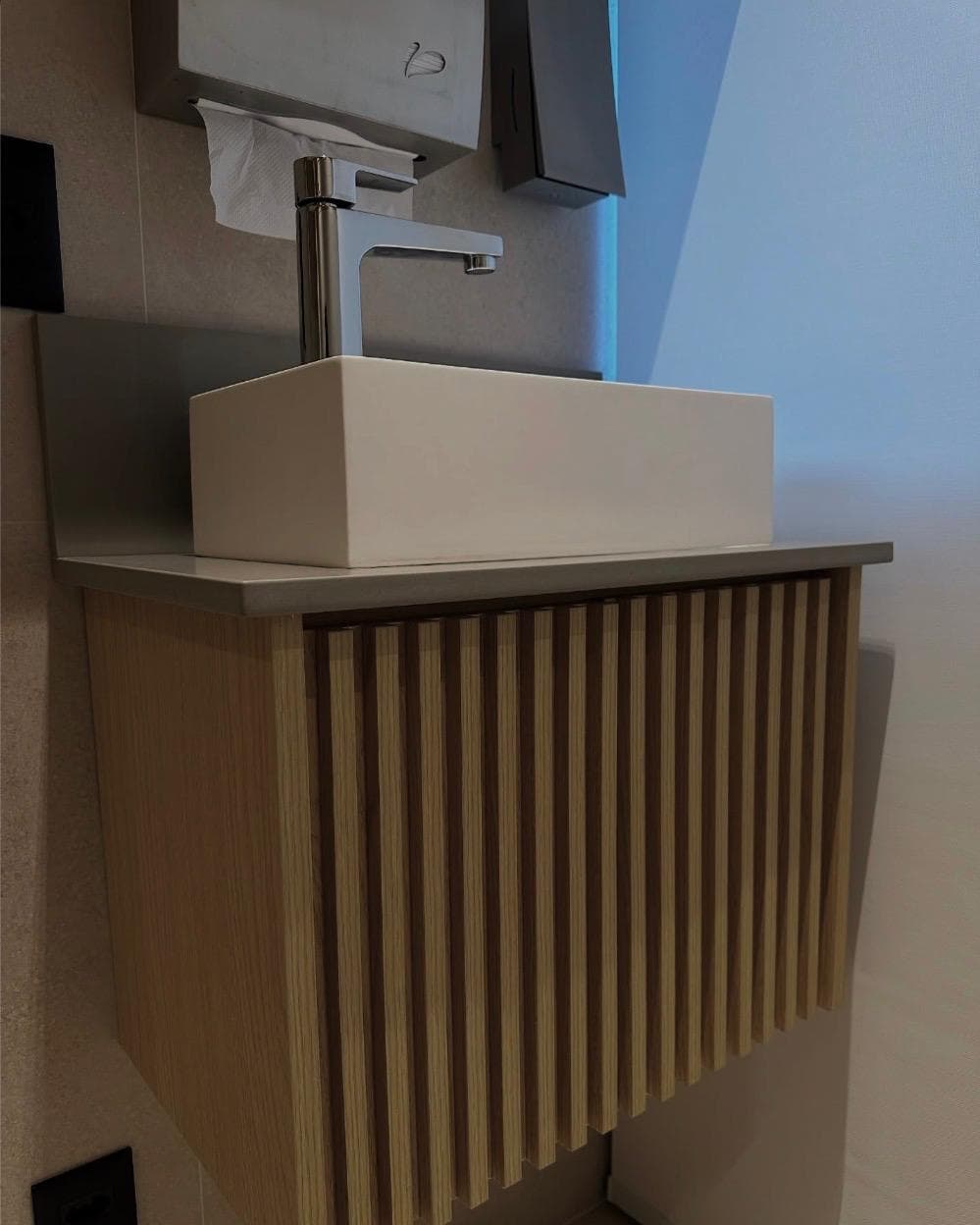 A wall-hung powder room vanity with a slatted oak front, stone top and a square vessel basin.